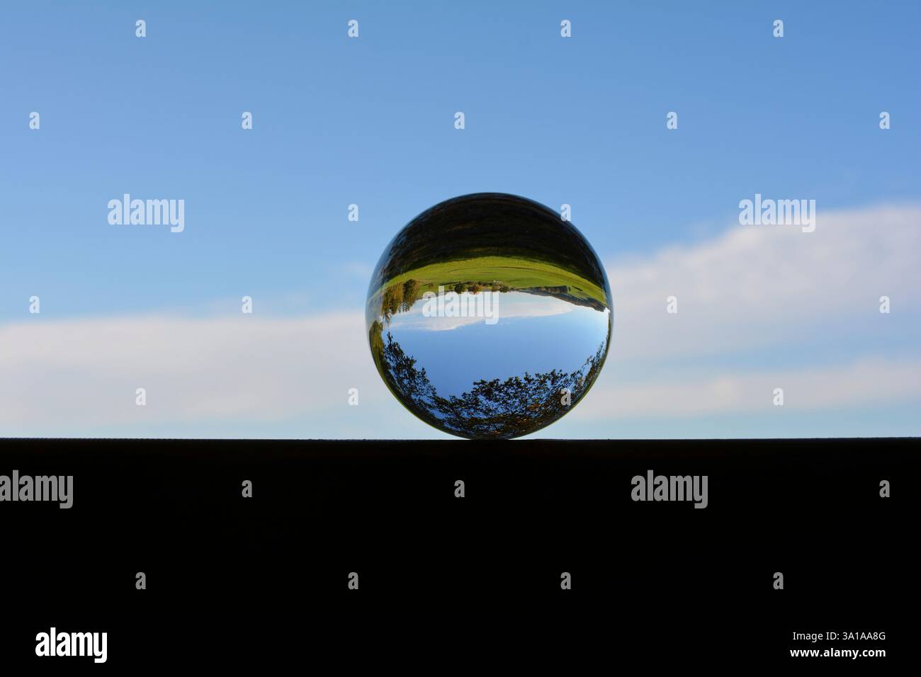 Sfera di vetro su legno in natura, con riflessi di un paesaggio verde in vetro, con cielo blu Foto Stock