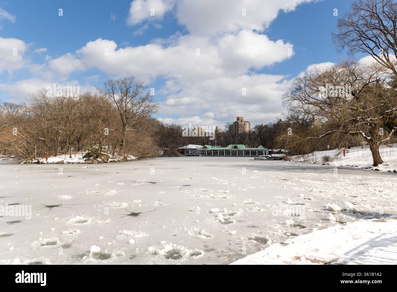 10/2/2025, New York, New York, Stati Uniti – Una serena vista invernale del lago coperto di neve di Central Park con la Boathouse visibile come una sottile striscia al centro, Foto Stock