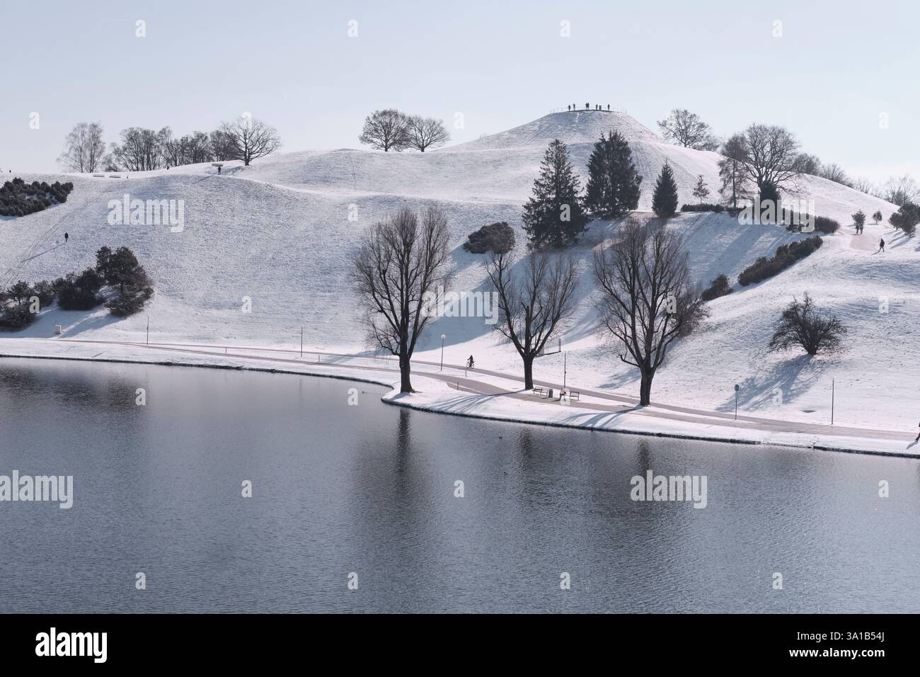 Olympiaberg a Monaco in una giornata invernale di sole. C'è un po' di neve, l'acqua del lago non è più ghiacciata e ci sono alcuni passanti e atleti fuori e intorno Foto Stock