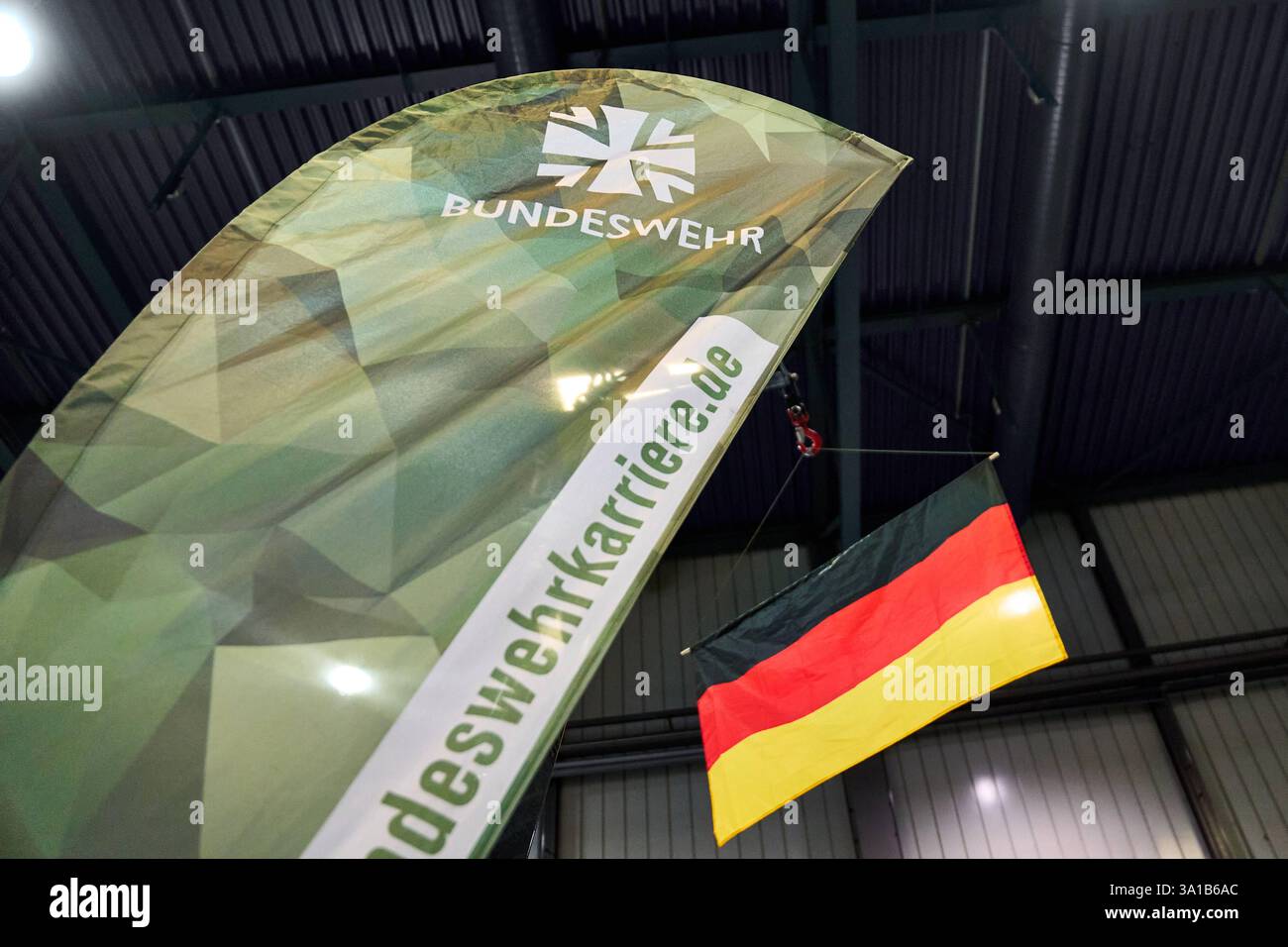 Augusta, Baviera, Germania - 7 marzo 2025: Stand della Bundeswehr alla fiera AFAIR di Augusta. Una bandiera della Bundeswehr con motivo mimetico e la bandiera tedesca *** Bundeswehr-Messestand auf der AFAIR Messe ad Augusta. Eine Bundeswehr-Fahne mit Tarnmuster und die deutsche Flagge Foto Stock