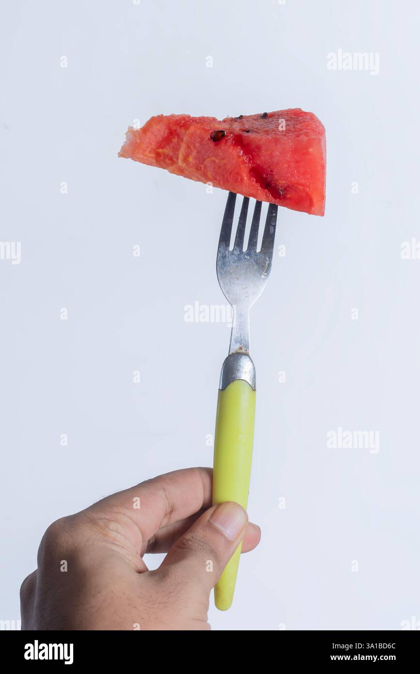 Una vivace e succosa fetta triangolare di anguria tenuta su una forchetta con un manico giallo. ideale per mangiare sano e temi tropicali. Foto Stock