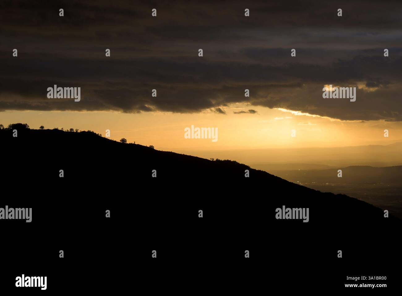 Collina retroilluminata all'alba con dettagli di alberi in una giornata nuvolosa in orizzontale Foto Stock