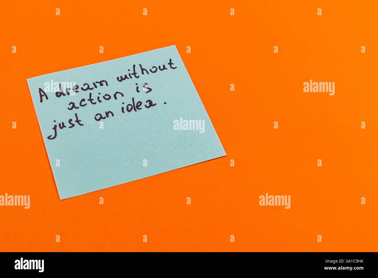 Una nota adesiva azzurra mostra una citazione ispiratrice sui sogni e l'azione. Lo sfondo è un arancione brillante, che aggiunge energia visiva al messaggio Foto Stock