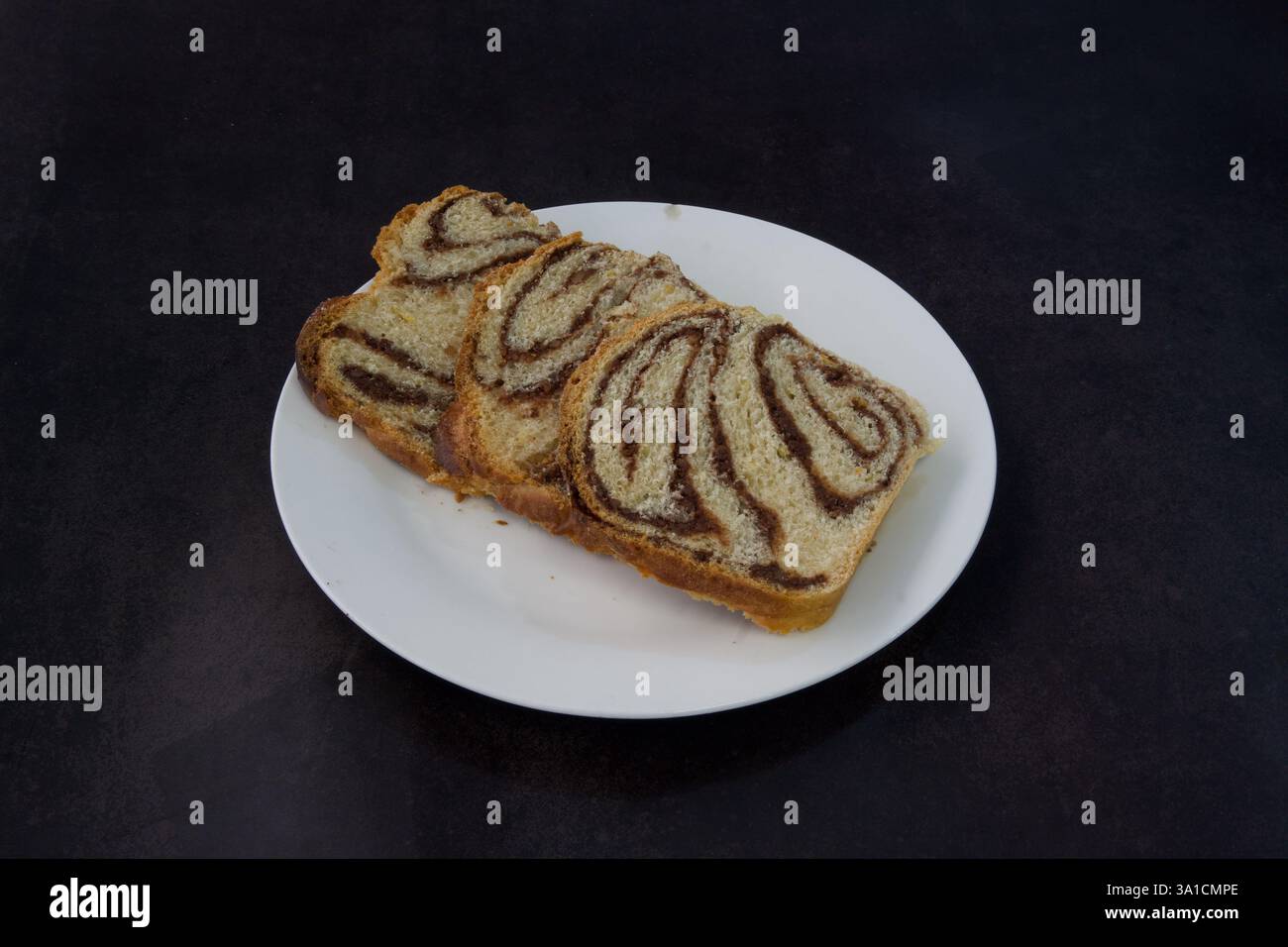 Tre fette di pane con giravolte di cioccolato su un piatto bianco. La piastra si trova su una superficie scura Foto Stock
