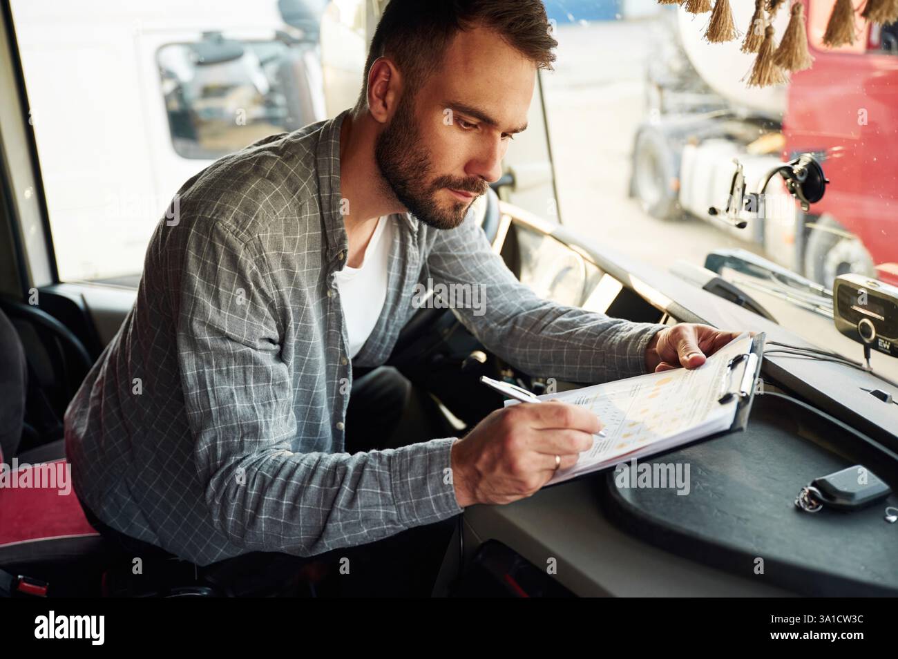 Scrivere nel documento, seduto all'interno. Giovane camionista con abiti casual. Foto Stock