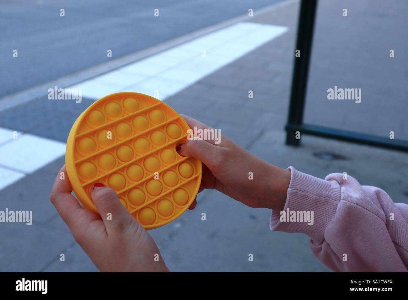Mani femminili che giocano con un giocattolo giallo. Braccio o maglietta rosa che regge il dispositivo in plastica. Primo piano e isolato. Foto Stock