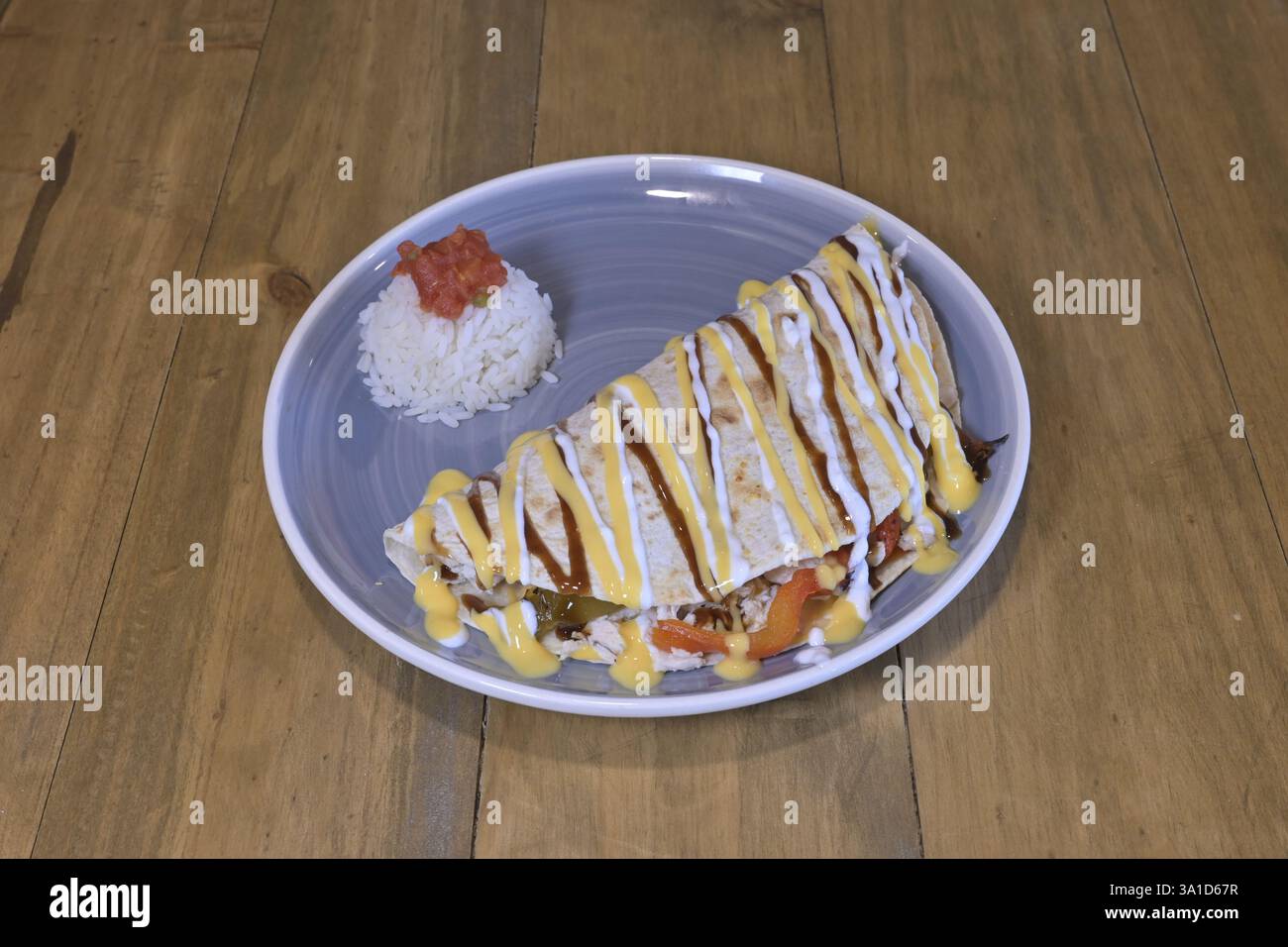 Un piatto di cibo con burrito e riso sopra. Il burrito è ricoperto da una salsa gialla Foto Stock
