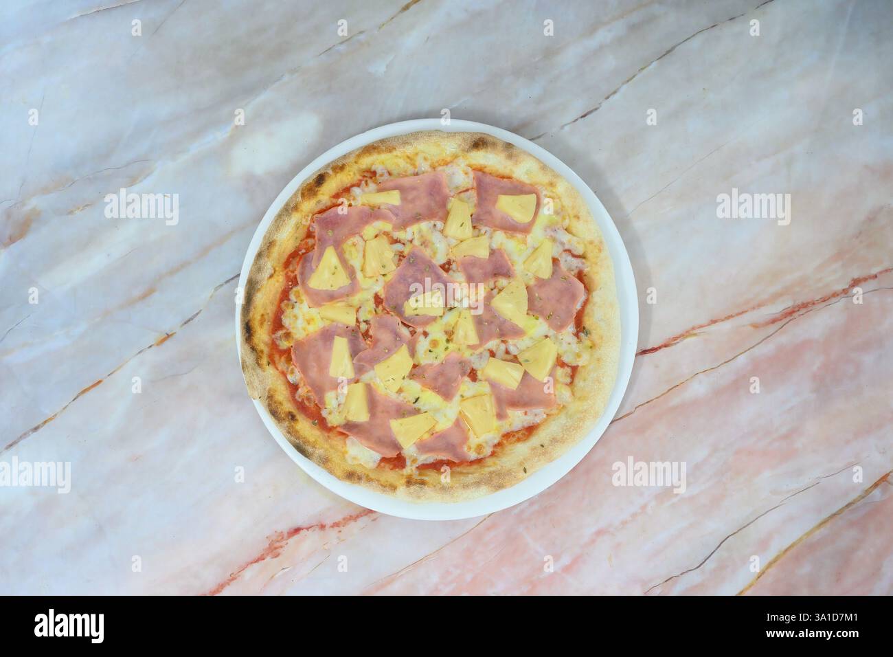 Una pizza con prosciutto e ananas su un piatto bianco. La pizza è collocata su un ripiano di marmo Foto Stock