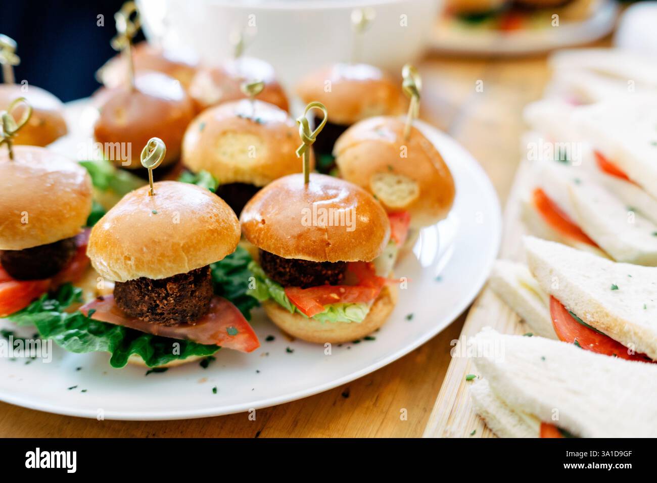 Succulenti mini cheeseburger serviti su un piatto splendidamente guarniti con lattuga e fette di pomodoro, ideali per feste, antipasti o finger food. Foto Stock