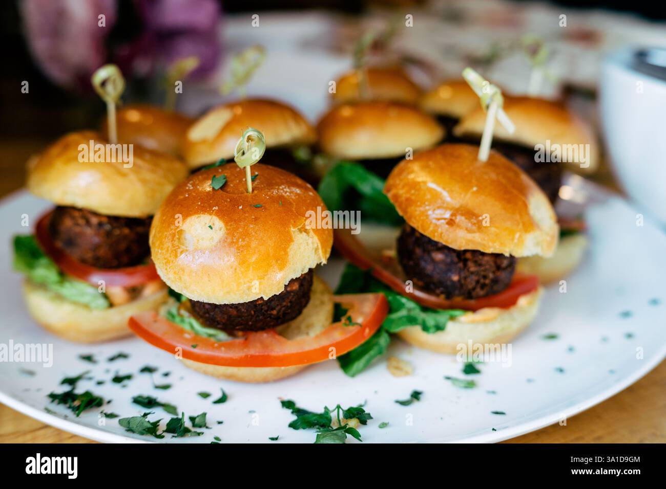 Succulenti mini cheeseburger serviti su un piatto splendidamente guarniti con lattuga e fette di pomodoro, ideali per feste, antipasti o finger food. Foto Stock