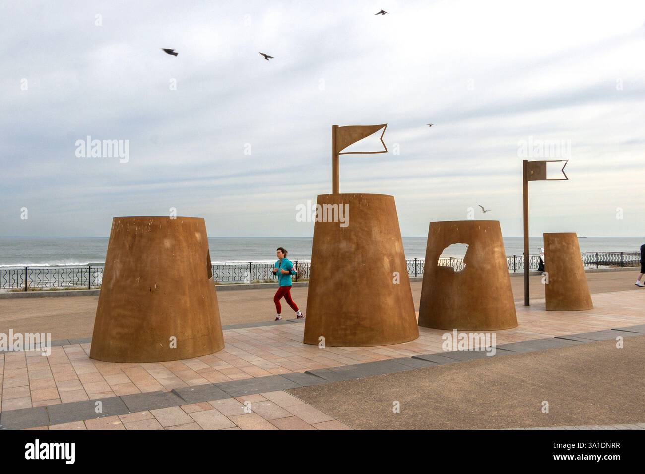 Donne che passano per corten in acciaio sandcastle sculture installazione artistica artista Richard Broderick Promenade città spagnola whitley Bay tyne & Wear regno unito Foto Stock