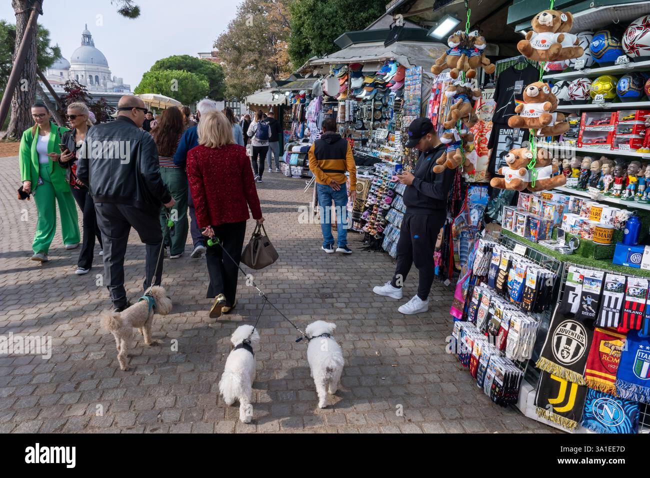 Venezia, Italia - 12 ottobre 2024: I turisti curiosano in uno stand di souvenir che vende maschere veneziane, portachiavi e altri cimeli Foto Stock