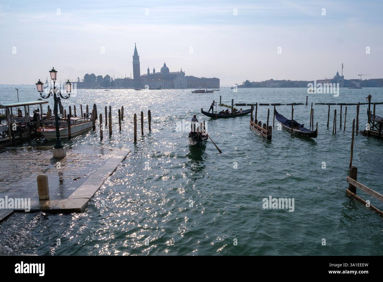 Venezia, Italia - 12 ottobre 2024: Gondole tradizionali che navigano nelle scintillanti acque della laguna veneta vicino a San Giorgio maggiore Foto Stock