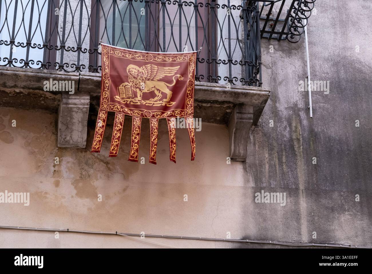 Venezia Italia – 7 ottobre 2023 bandiera veneziana rossa e dorata con il Leone di San Marco appeso da uno storico balcone su una facciata di un edificio intempestivo Foto Stock