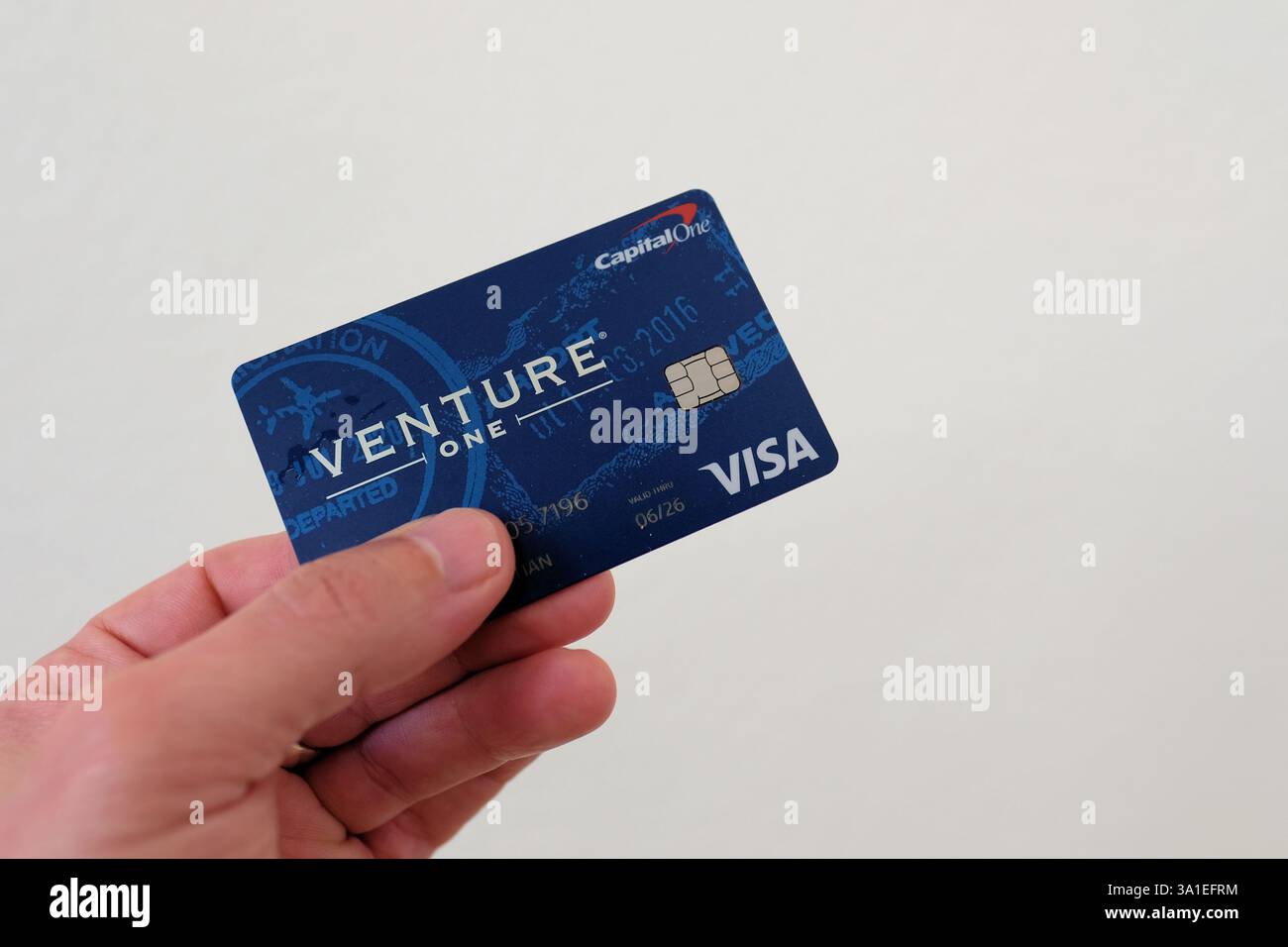 Mano con una sola carta di credito Venture One Visa su sfondo bianco; sistema di credito, bancario e finanziario Capital One. Foto Stock