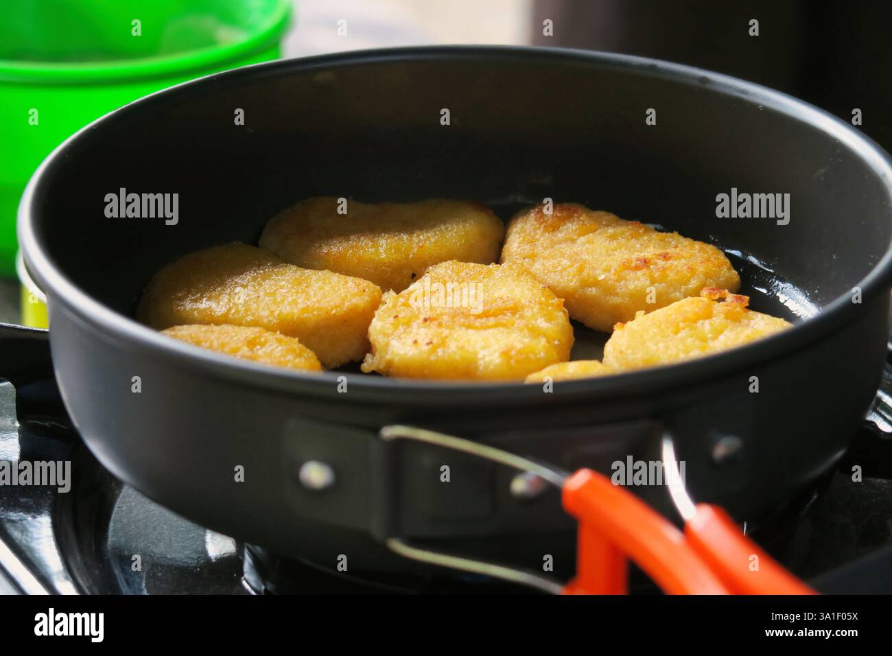 Una padella con diverse pepite di pollo dorate cotte su un piano cottura. Foto Stock