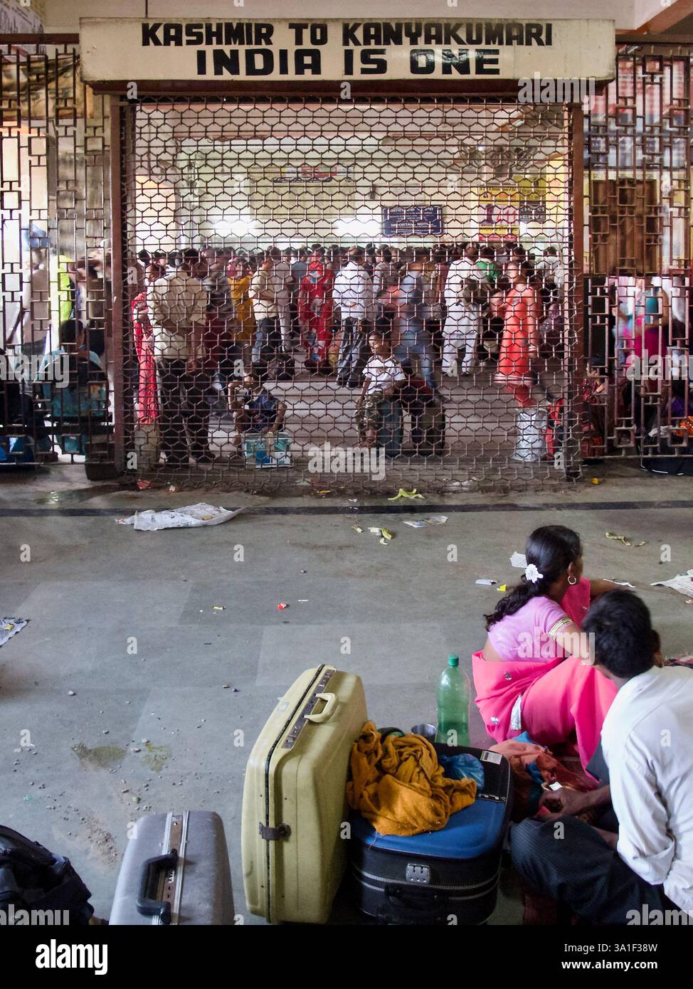 Le famiglie riposano sul pavimento della stazione ferroviaria di Varanasi vicino a un cartello con la scritta "Kashmir to Kanyakumari, India is One" nella sala d'attesa. Foto Stock