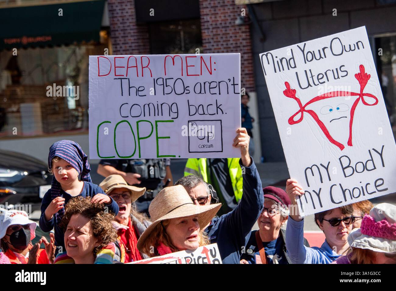 San Francisco, Stati Uniti. 8 marzo 2025. Centinaia di persone si radunano per protestare e protestare in onore della giornata internazionale della donna a Union Square di San Francisco. Una donna porta un bambino sulle spalle mentre altri nella folla tengono dei cartelli che recitano: "Cari uomini: Gli anni '1950 non tornano. COPE, e 'Mind Your own uterus, My Body My Choice'. Crediti: Shelly Rivoli/Alamy Live News Foto Stock