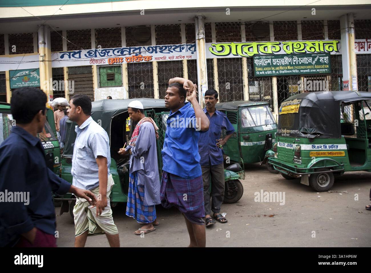 Uomini musulmani che indossano lungi e camicia in piedi a tempo verde in risciò auto fuori dal terminal delle barche Sadarghat, Dacca, Bangladesh, Asia Foto Stock