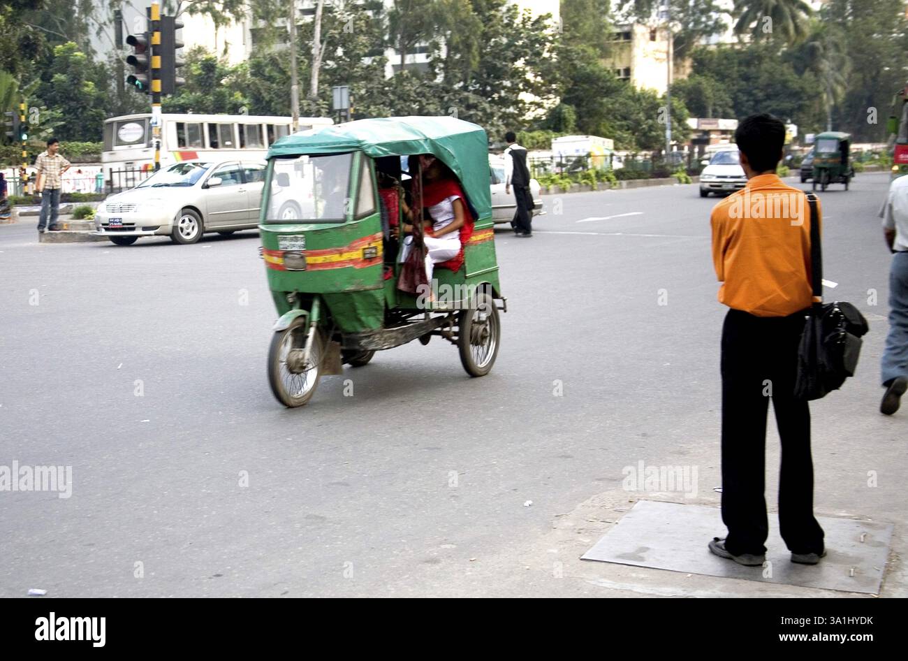 Scena di strada, uomo di passaggio in risciò di colore verde che indossa una camicia arancione in piedi sulla strada, Dacca, Bangladesh, Asia Foto Stock
