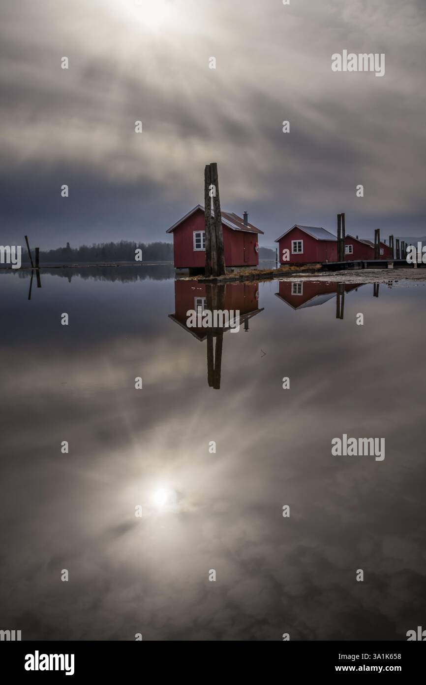 Le vecchie passerelle in legno e le boatouses rosse si riflettono nell'acqua poco profonda, raccontando storie di tempo che passa Foto Stock