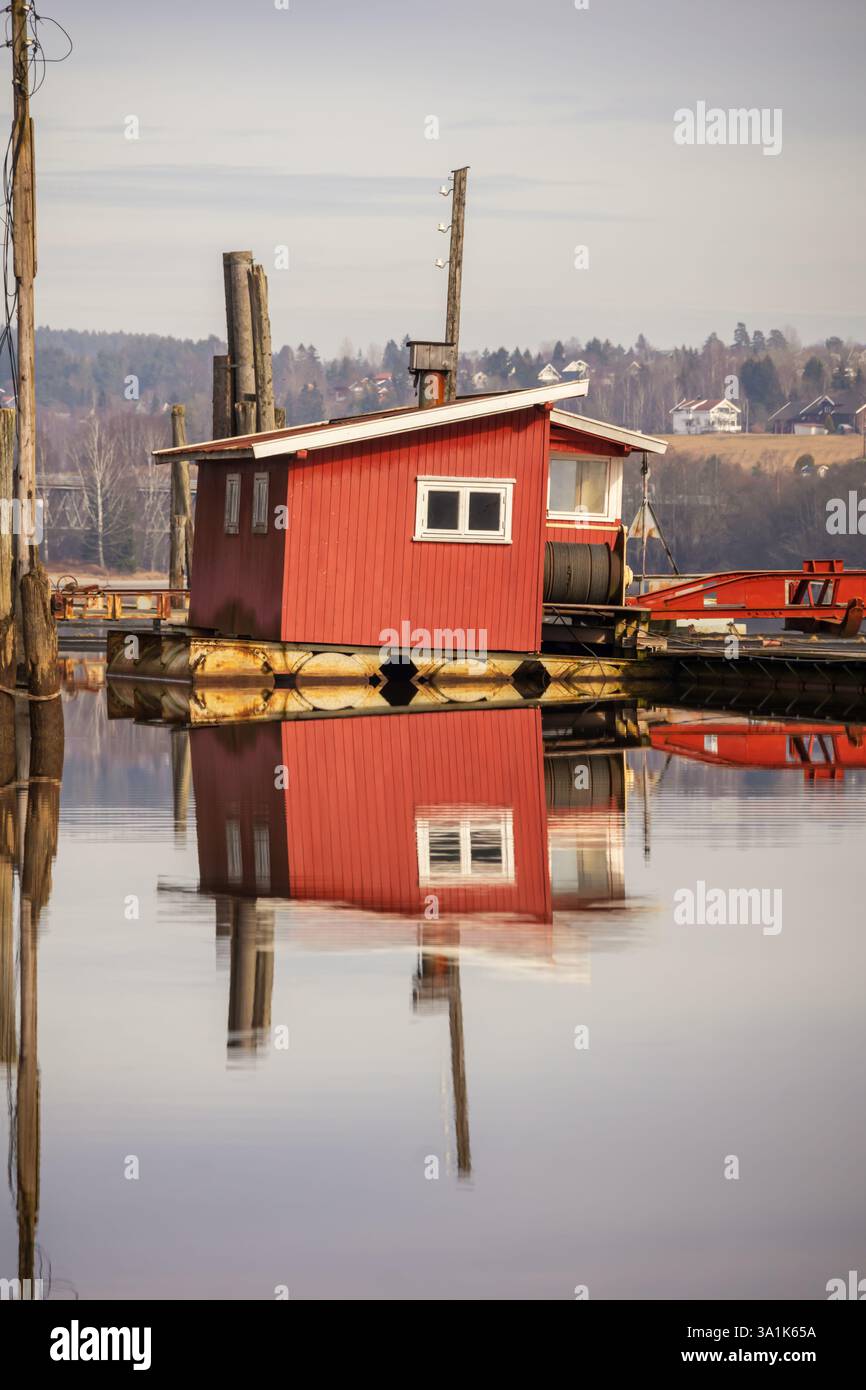 Le vecchie passerelle in legno e le boatouses rosse si riflettono nell'acqua poco profonda, raccontando storie di tempo che passa Foto Stock