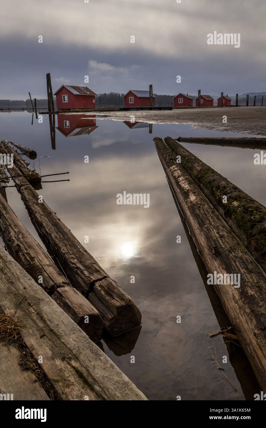 Le vecchie passerelle in legno e le boatouses rosse si riflettono nell'acqua poco profonda, raccontando storie di tempo che passa Foto Stock