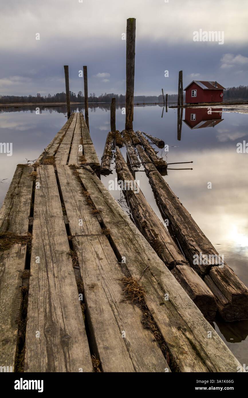 Le vecchie passerelle in legno e le boatouses rosse si riflettono nell'acqua poco profonda, raccontando storie di tempo che passa Foto Stock