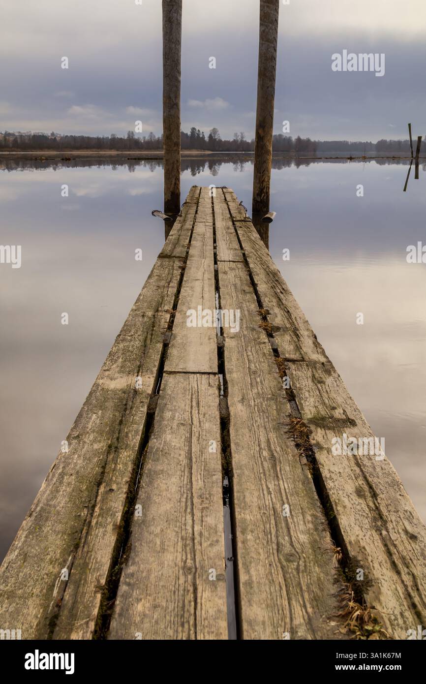Le vecchie passerelle in legno e le boatouses rosse si riflettono nell'acqua poco profonda, raccontando storie di tempo che passa Foto Stock