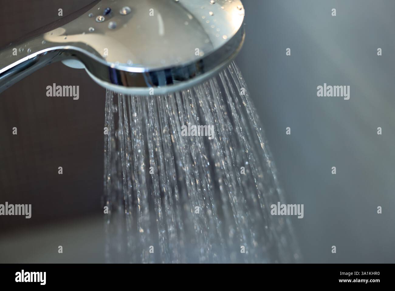 Primo piano di una doccia cromata portatile che spruzza acqua, con gocce e riflessi visibili. Foto Stock