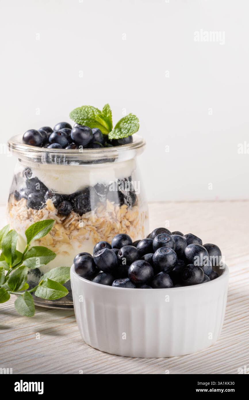 Mirtillo fresco in ciotola e yogurt con muesli e mirtillo forestale e menta in un vaso di vetro sana colazione biologica con probiotici Berry parfait Foto Stock