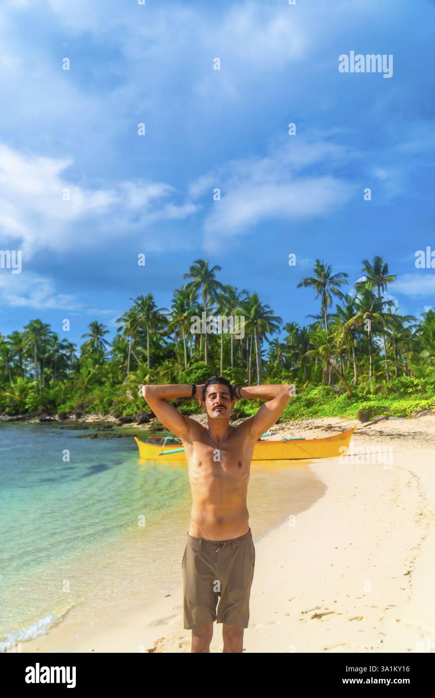 Giovane che si gode una vacanza estiva su una splendida spiaggia dell'isola di cawhagan, nelle filippine, circondato da acque cristalline e palme Foto Stock