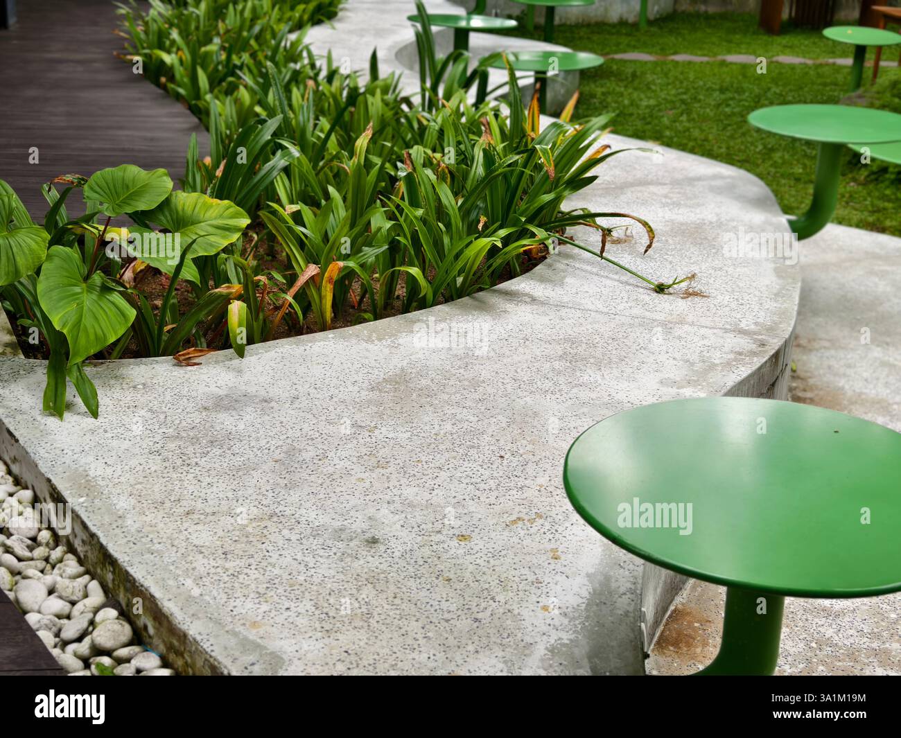 Una panca curva in cemento con vegetazione incorporata e tavoli rotondi verdi attaccati negli spazi pubblici esterni Foto Stock