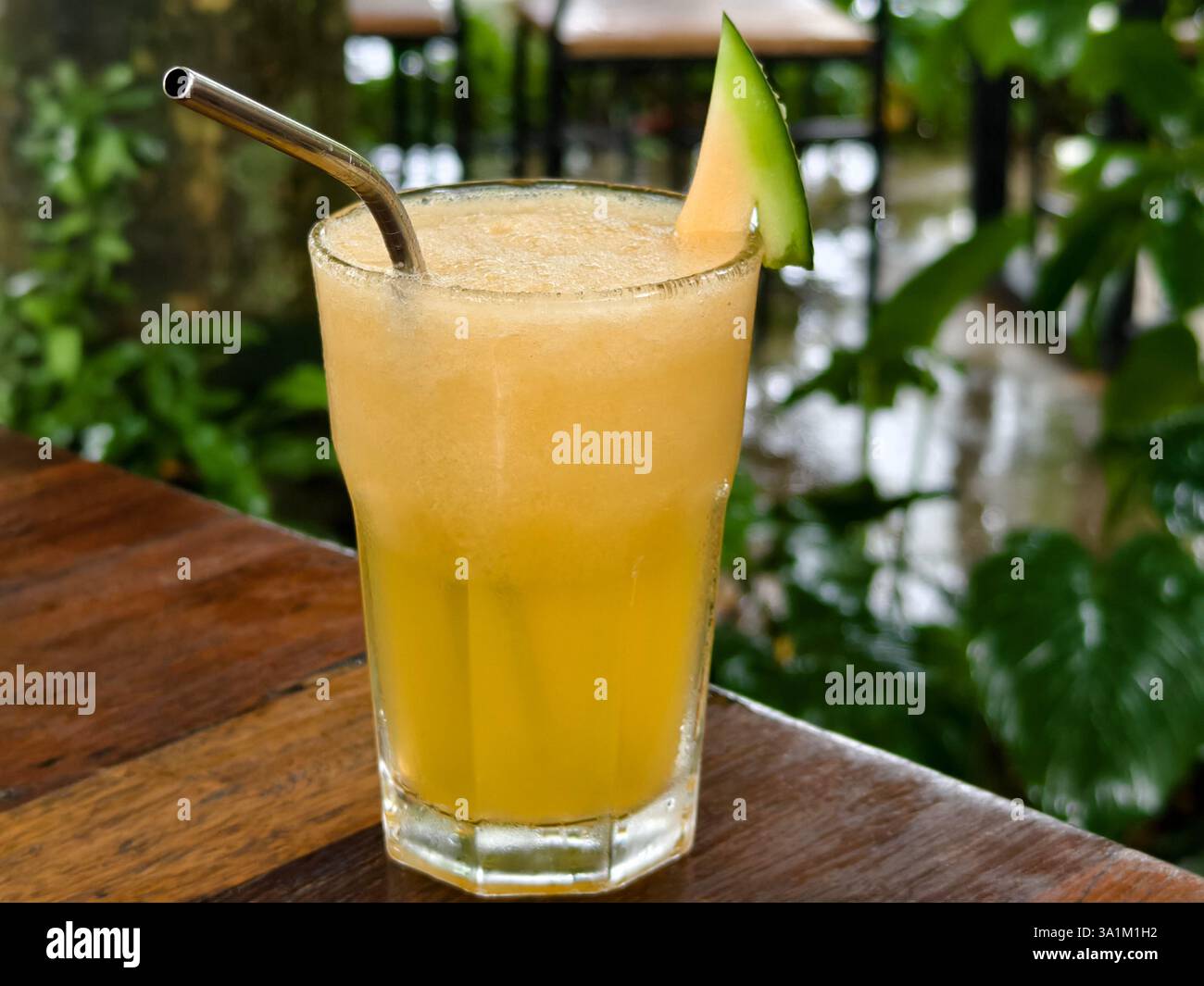 Un succo di melone frullato a freddo guarnito con una fetta di melone e una cannuccia di metallo riutilizzabile Foto Stock