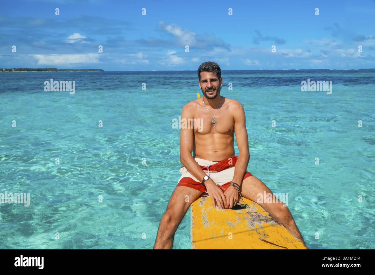 Giovane uomo che si rilassa su una barca gialla banca nel mare tropicale turchese dell'isola di daku, siargao, filippine, godendo delle vacanze estive Foto Stock