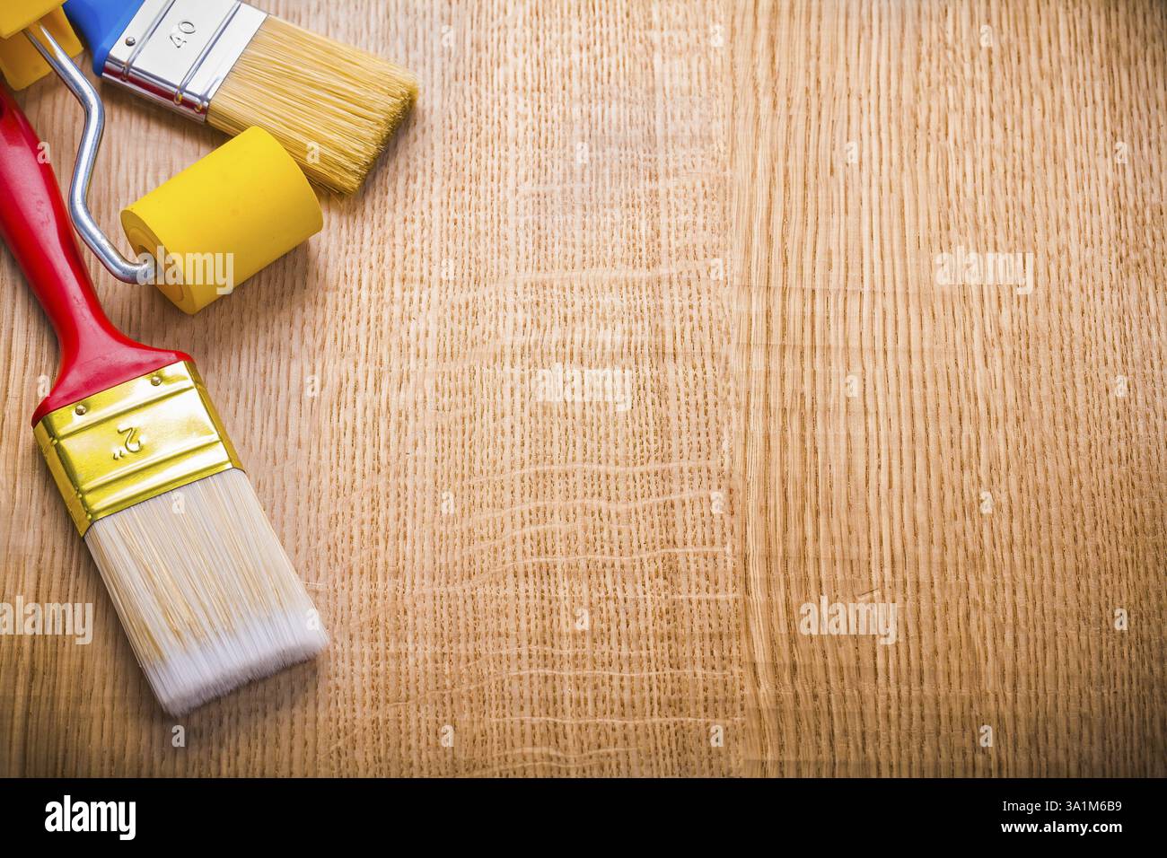 Copyspace organizzato due pennelli e rullo su tavola di legno Foto Stock