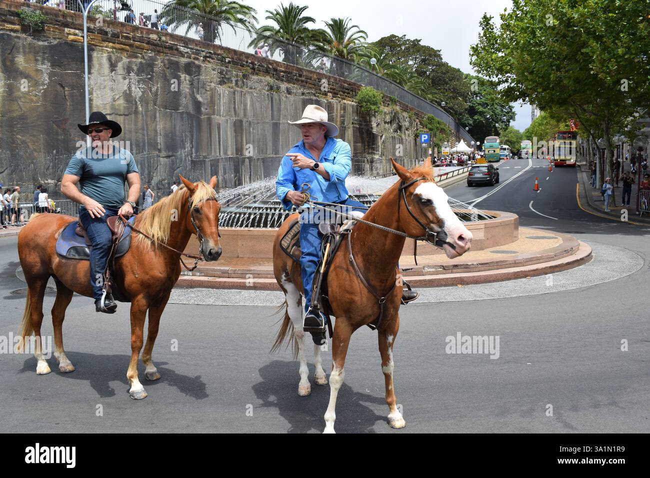 Scena unica di due cowboy che cavalcano un cavallo per le strade urbane di Sydney, mescolando il fascino occidentale con il vibrante paesaggio urbano dell'Australia. Foto Stock