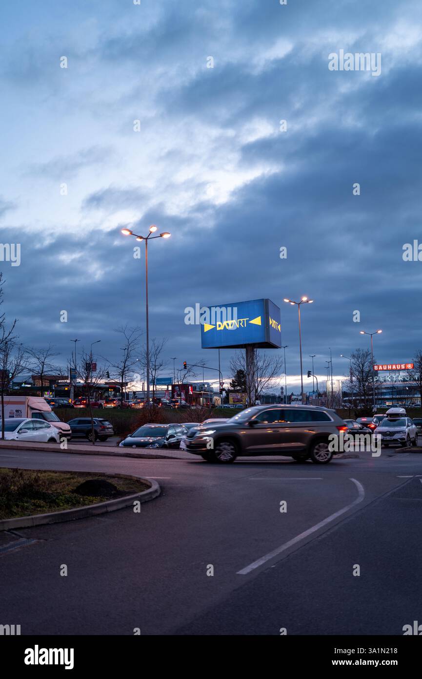 Traffico serale in una trafficata rotatoria di Praga con cartellone illuminato, semafori e cielo nuvoloso al tramonto Foto Stock