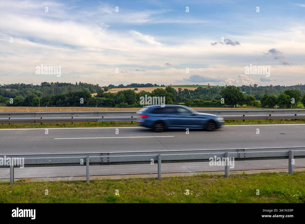 Auto blu che guida velocemente sull'autostrada ceca con movimento sfocato e campagna panoramica di alberi, campi e colline sullo sfondo Foto Stock