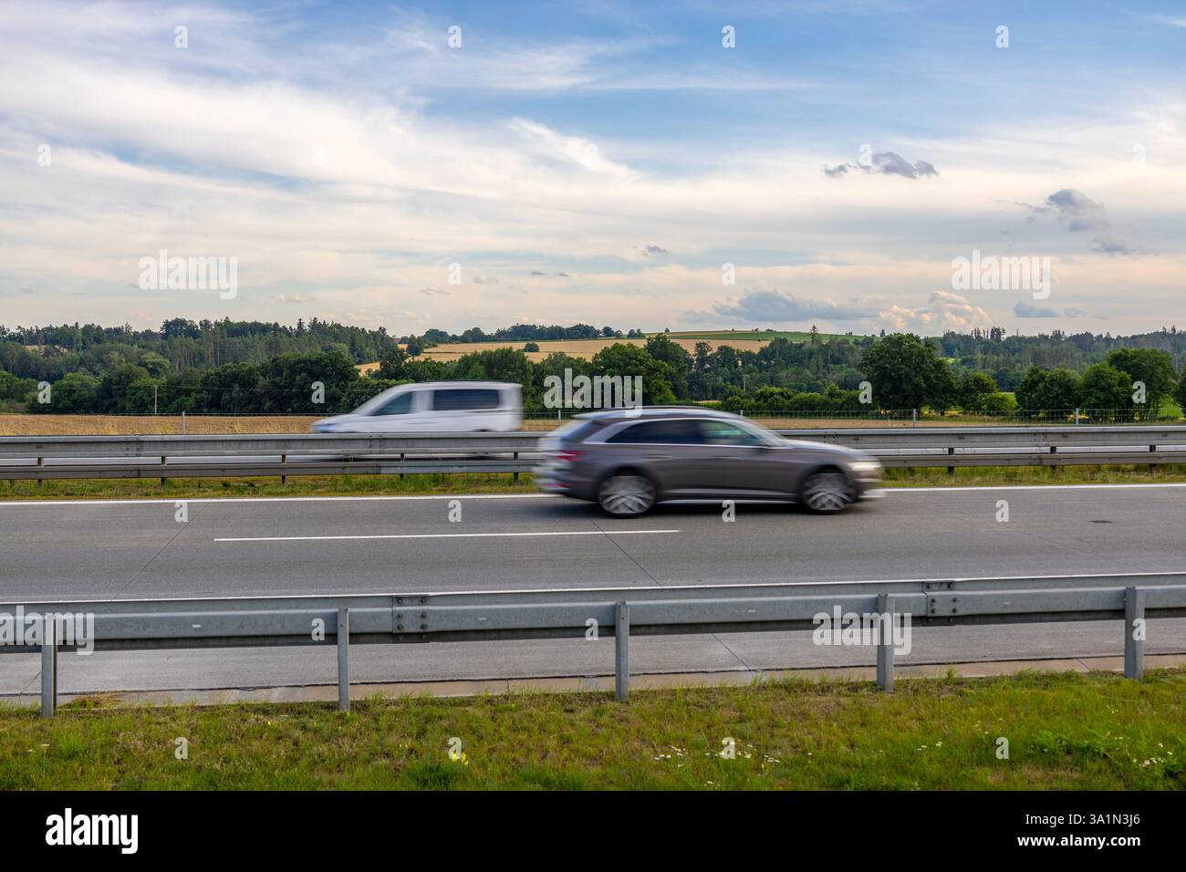 Due auto in movimento sull'autostrada ceca con campagna ondulata e terreni agricoli sullo sfondo sotto un cielo estivo parzialmente nuvoloso Foto Stock