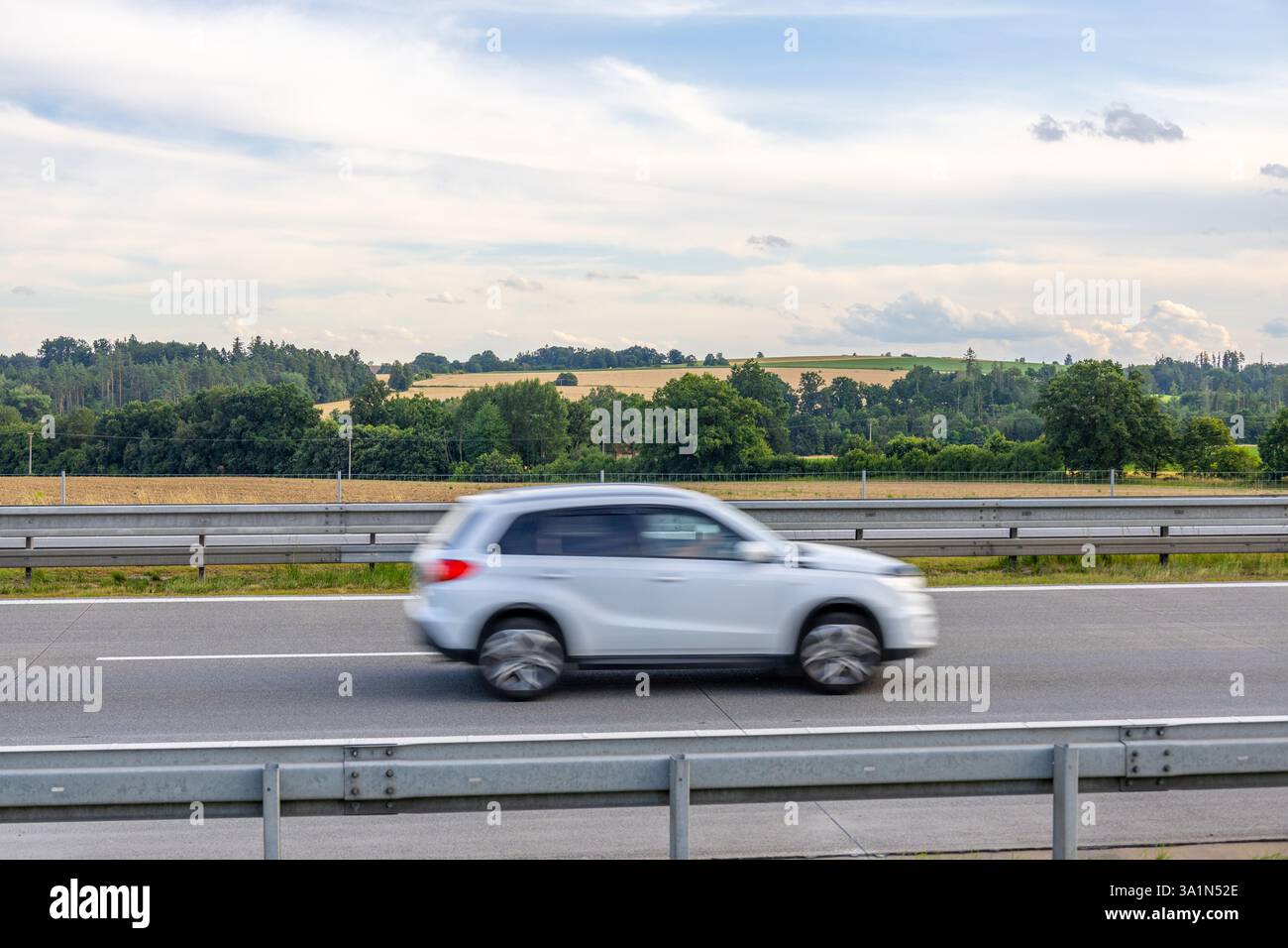Il White Suzuki Grand Vitara guida sull'autostrada ceca attraverso la campagna verde e dorata con foresta e nuvoloso cielo estivo sullo sfondo Foto Stock