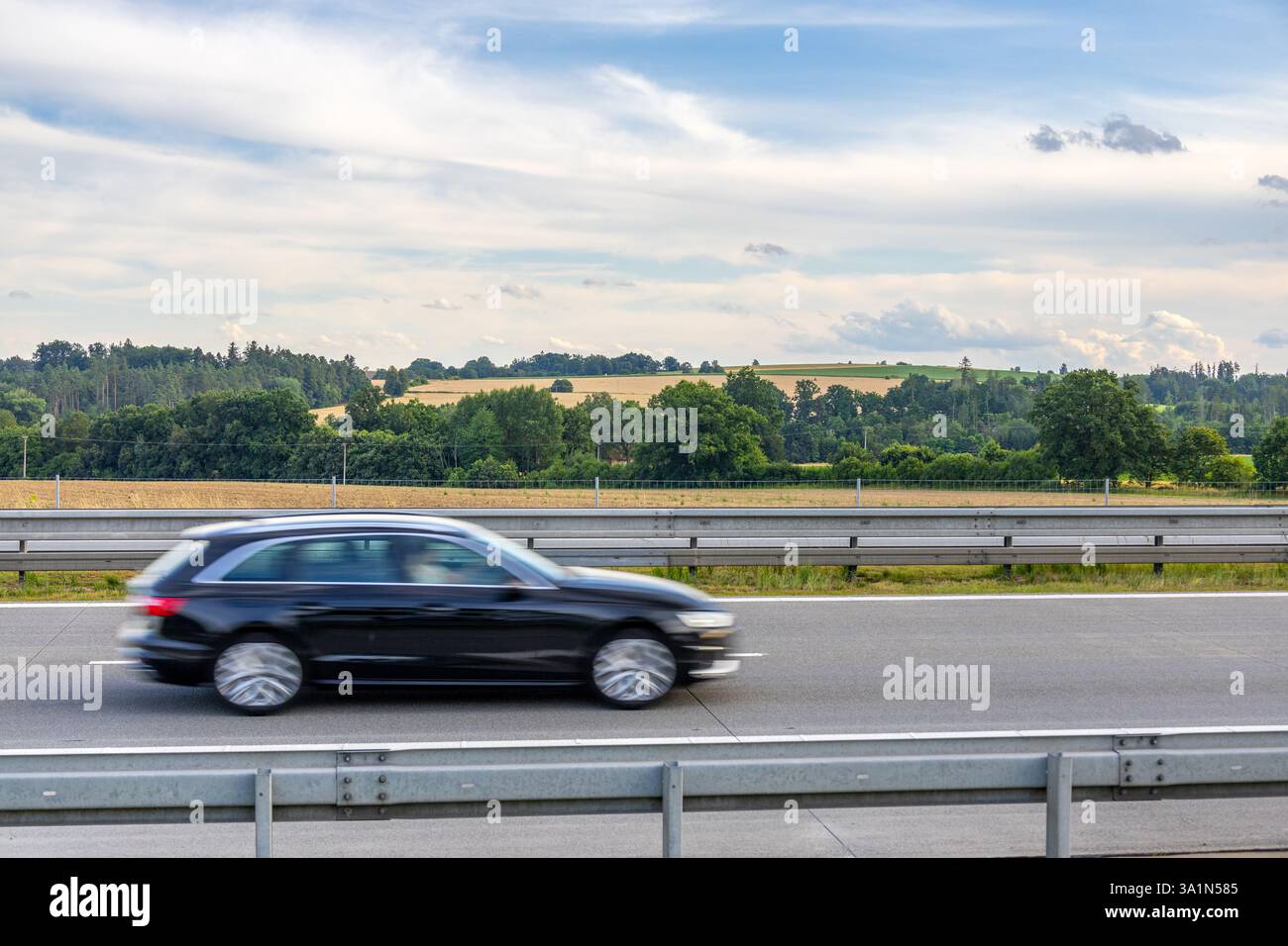 Audi A4 nera Avant in movimento sull'autostrada ceca con terreni agricoli verdi e gialli, alberi e nuvoloso cielo estivo sullo sfondo Foto Stock