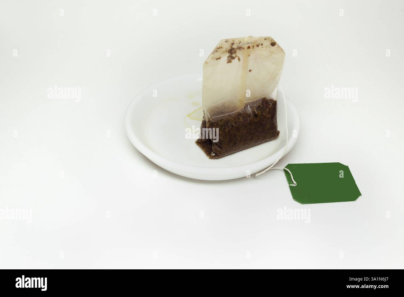 sacchetto di tè usato con filo lungo e carta verde, su un piccolo piattino bianco con macchie di tè Foto Stock