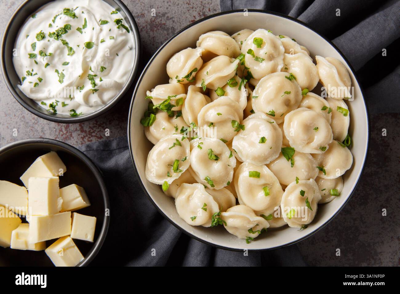 Gnocchi della cucina russa in una ciotola servita con panna acida, burro ed erbe da vicino sul tavolo. Vista dall'alto orizzontale Foto Stock
