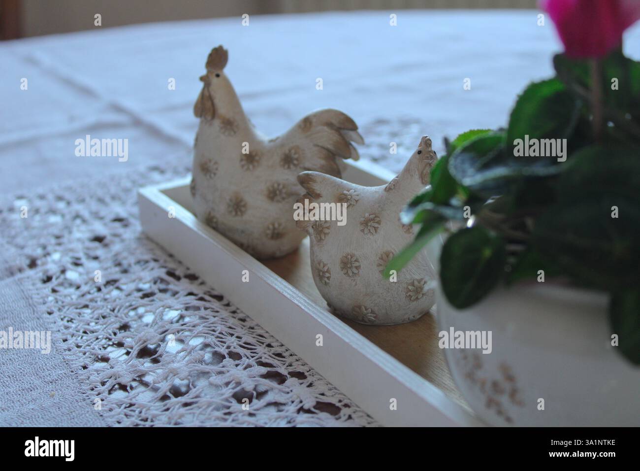 Decorazioni rustiche dei tavoli della fattoria con statuette di gallina in ceramica su un vassoio di legno, poste su una tovaglia di pizzo, a creare un'atmosfera accogliente in stile country. Foto Stock