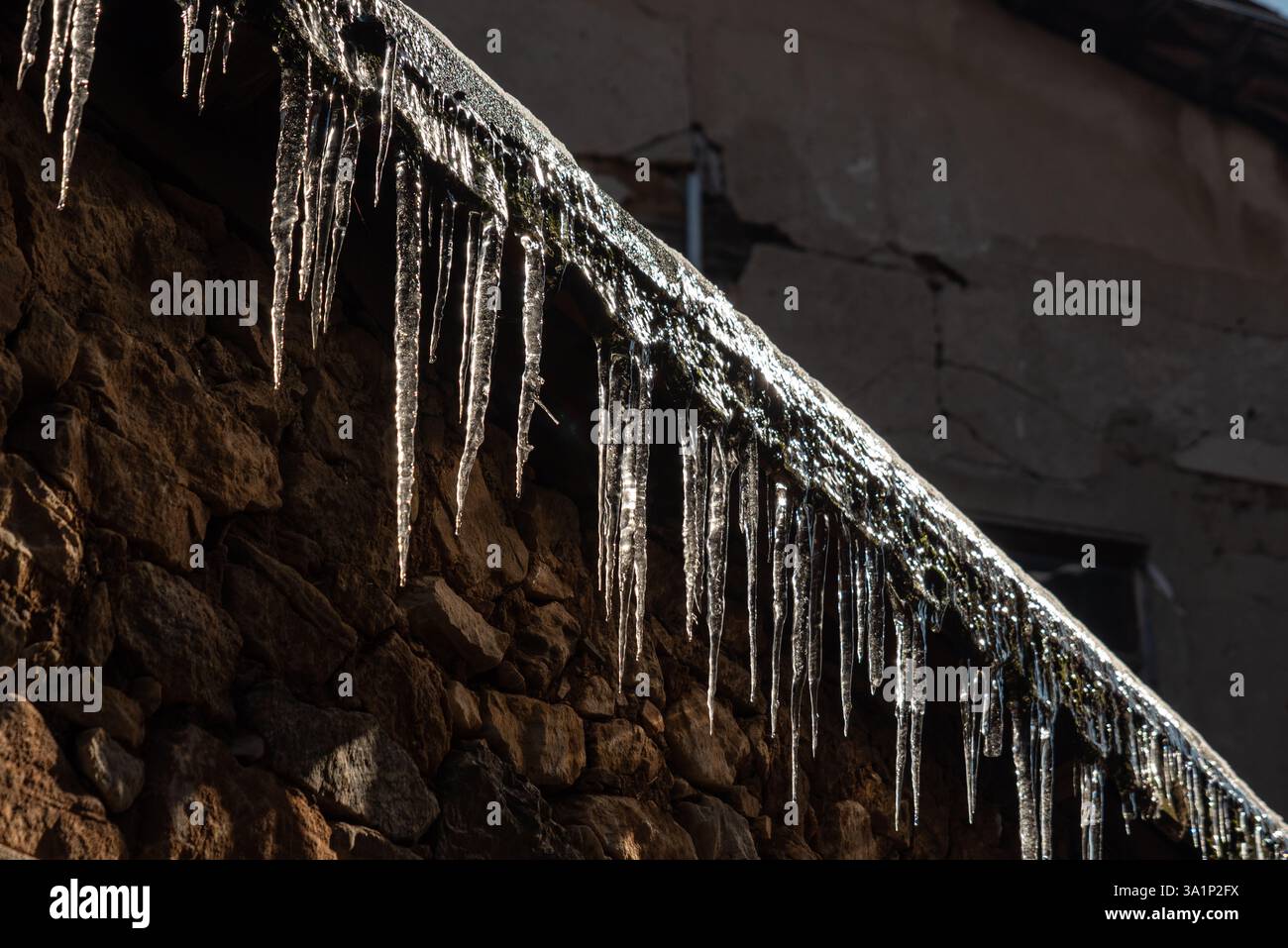 "Ghiaccioli sul tetto di una vecchia casa di pietra alla luce del sole d'inverno". Foto di alta qualità Foto Stock