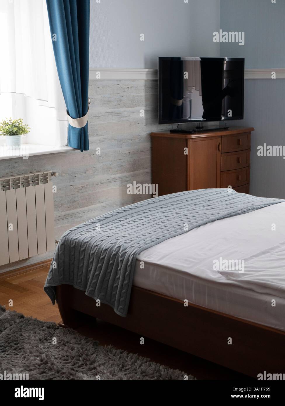 Camera da letto tranquilla con letto ben fatto, comò in legno e televisore. Concetto di tranquillità e comfort, importanza dello spazio personale e del riposo Foto Stock