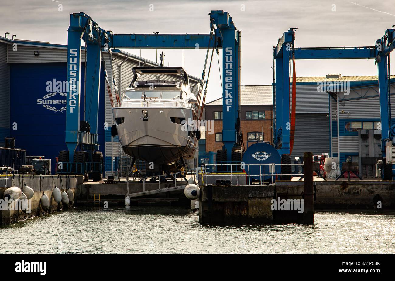 Yacht di lusso che viene sollevato in un cantiere navale con gru industriali ed edifici sullo sfondo Foto Stock