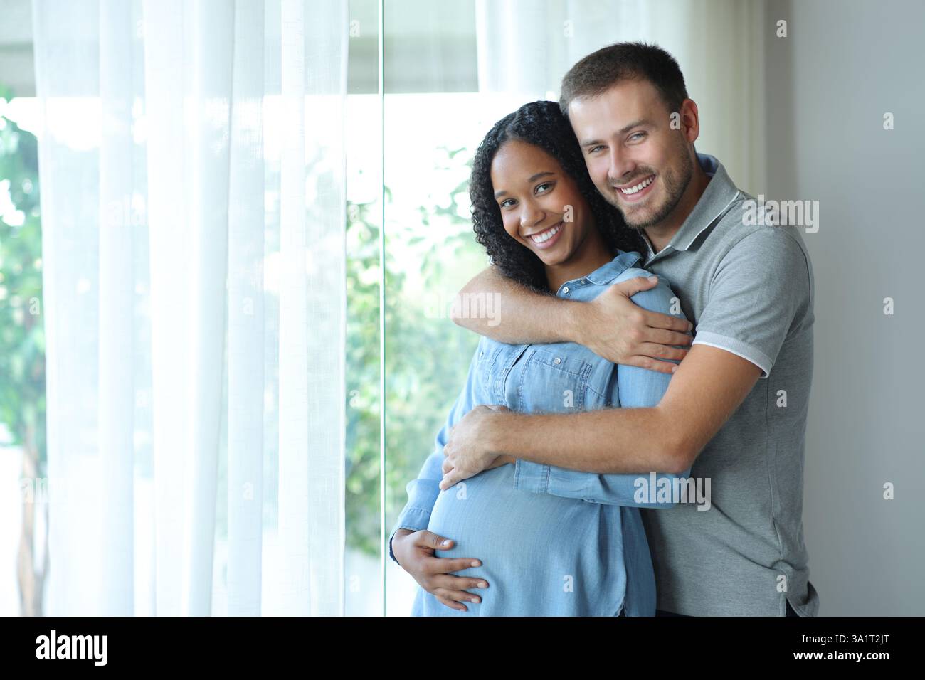 Donna incinta di colore e suo marito che guarda la macchina fotografica a casa Foto Stock