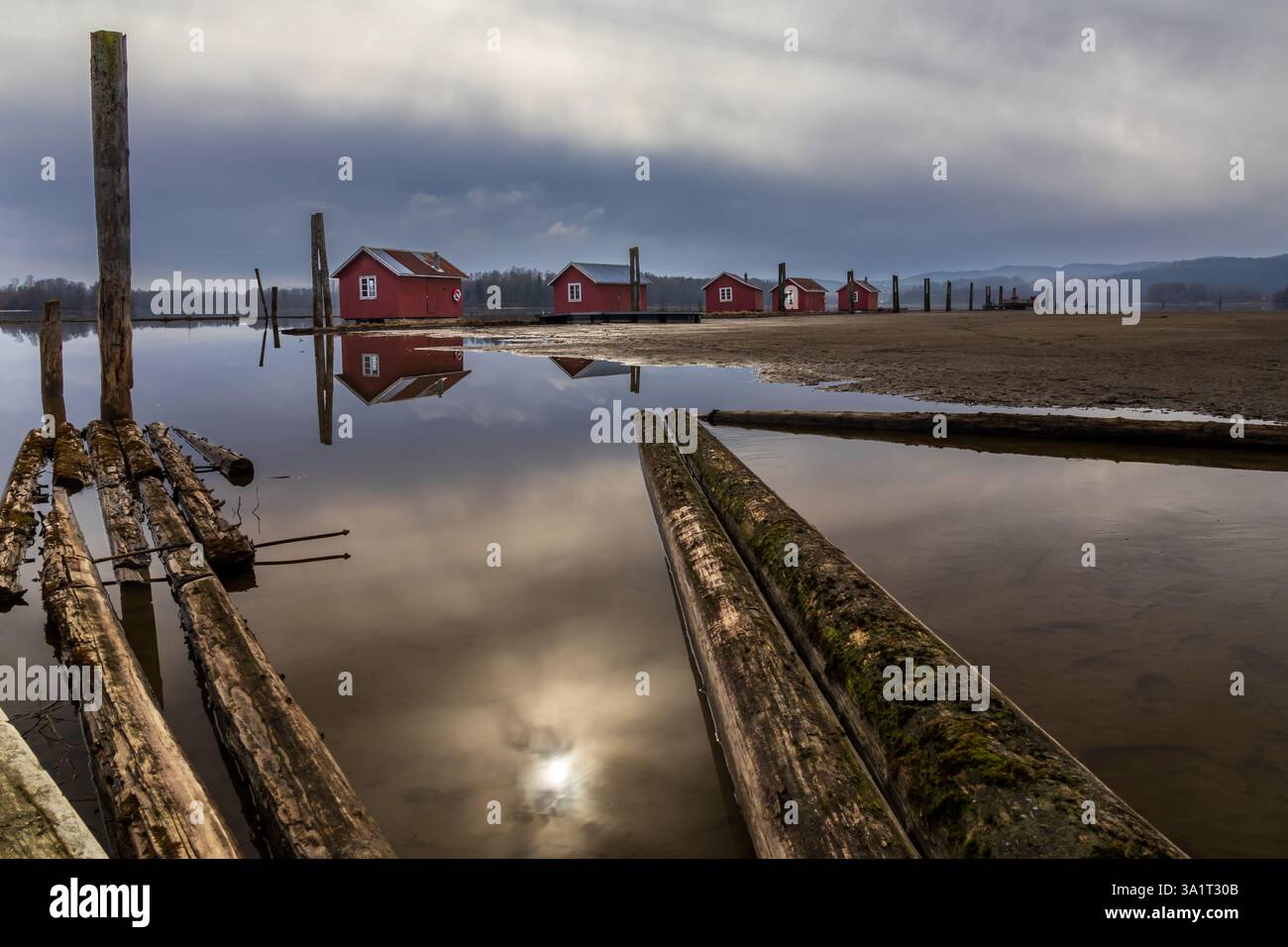 Le vecchie passerelle in legno e le boatouses rosse si riflettono nell'acqua poco profonda, raccontando storie di tempo che passa Foto Stock
